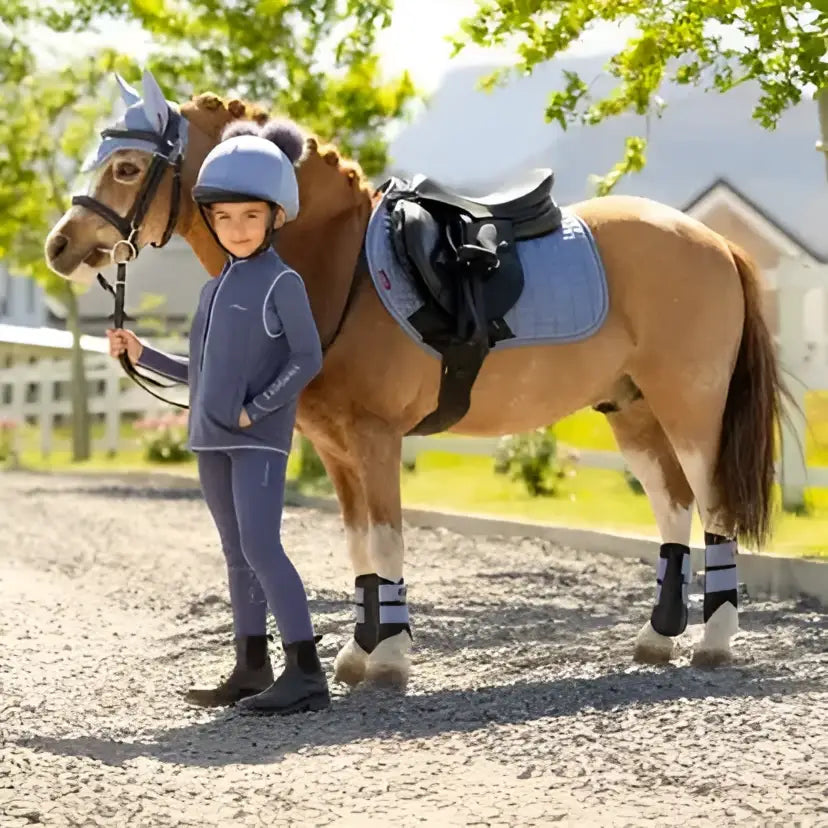 A young rider stands beside a chestnut horse wearing lemieux mini suede close contact square in powder blue