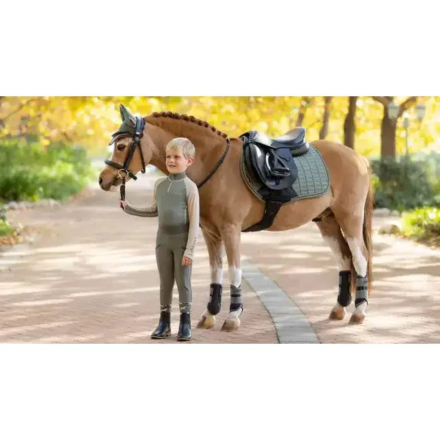 A young boy stands beside a chestnut horse wearing a lemieux mini suede contact square rosemary saddle pad in grey