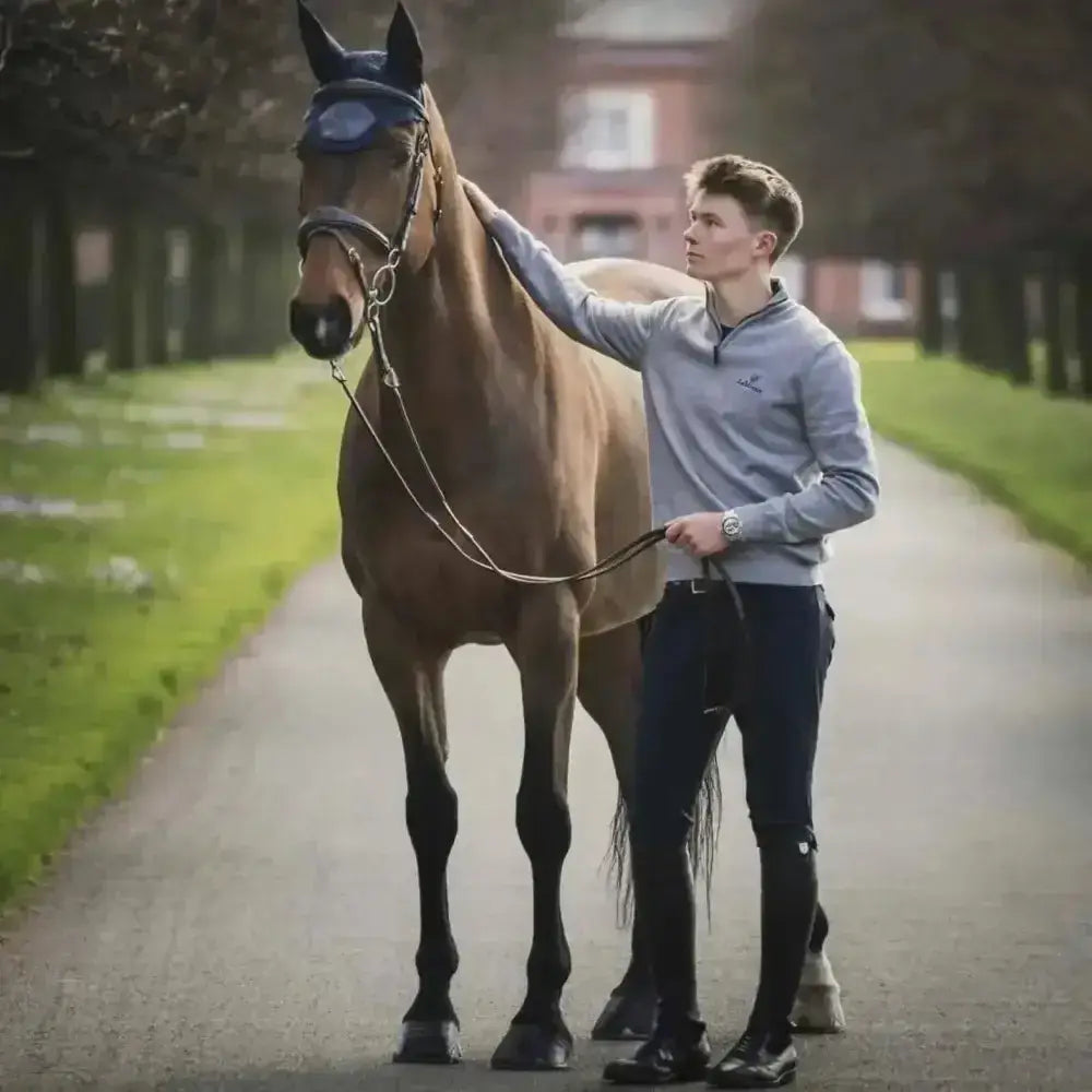 A sleek chestnut horse stands beside its handler wearing navy lemieux monsieur breeches for men with a comfy fit