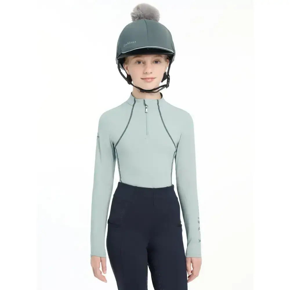 A sleek light green lemieux pippa hat silk long-sleeved equestrian top with black zipper and silky smooth four-way stretch