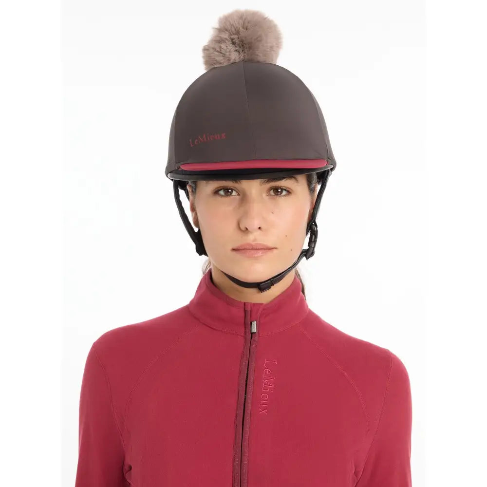Dark gray lemieux pom hat silk cinder equestrian helmet with pink trim and a fluffy brown pom-pom made from silky smooth four-way fabric
