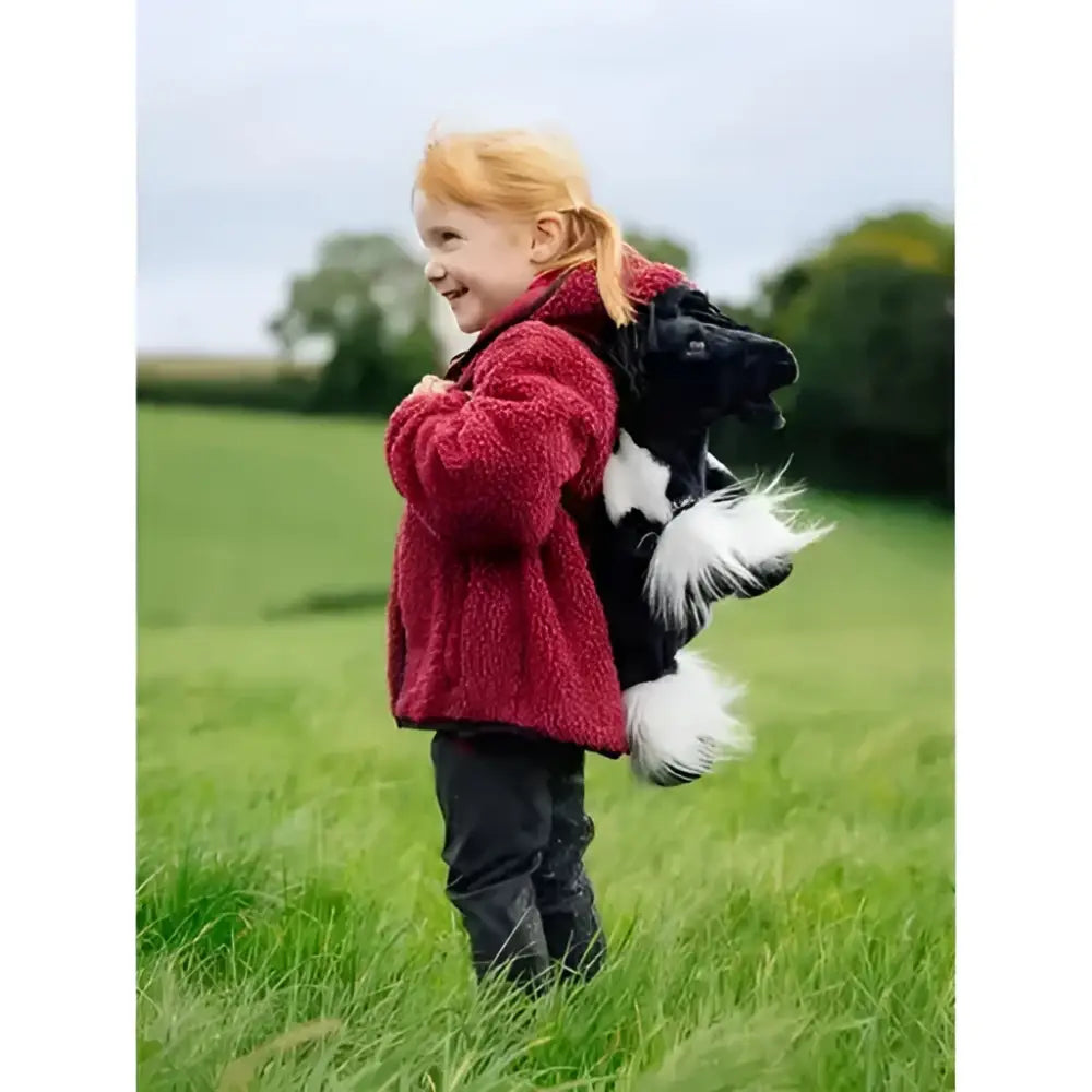 A child in a red fleece jacket carrying a fluffy black and white plush skunk toy with the lemieux pony bag razzle
