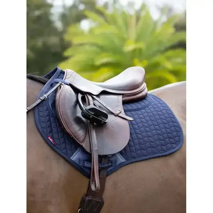 Brown leather saddle resting on a navy lemieux prosorb plain close contact square quilted horse pad