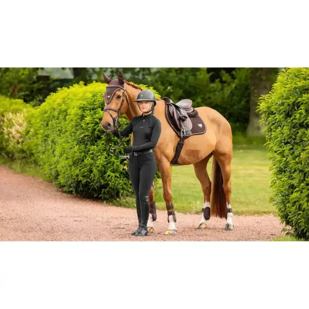 A chestnut horse with a brown lemieux puissance suede close contact square saddle stands beside its rider on a gravel path