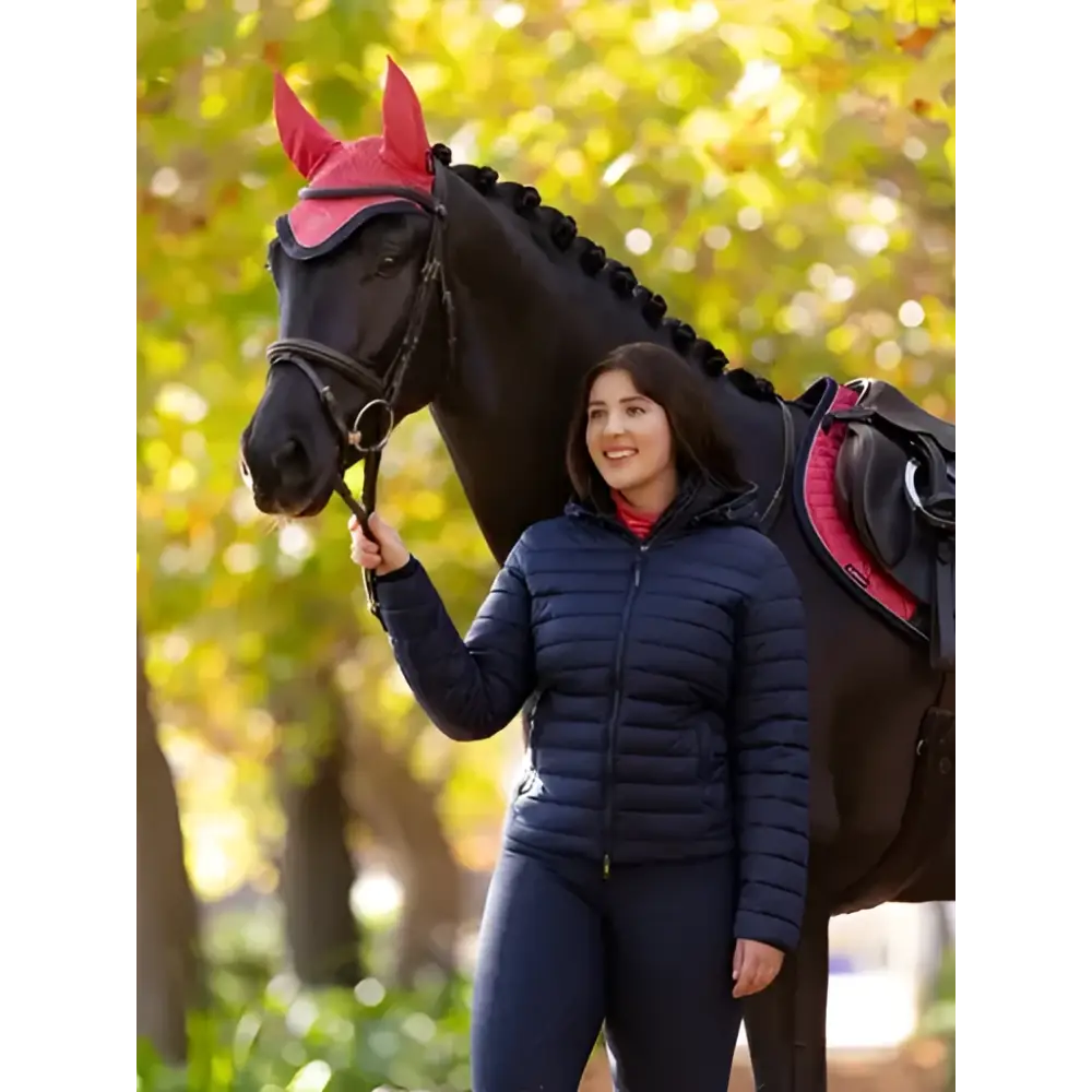 The horse wears a vibrant pink ear cover with pointed tips paired with a lemieux rose hooded puffer jacket navy