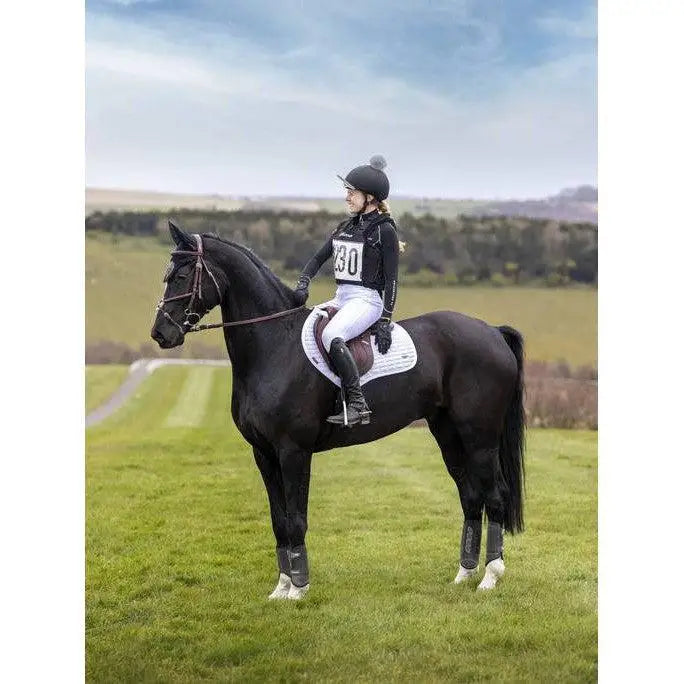 Black horse wearing lemieux self-cool close contact square arctic white saddle pad with rider in equestrian gear