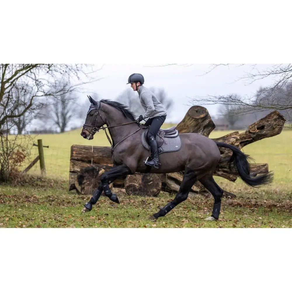 Dark gray horse wearing lemieux self-cool close contact saddle pad in square polar grey with protective leg wraps