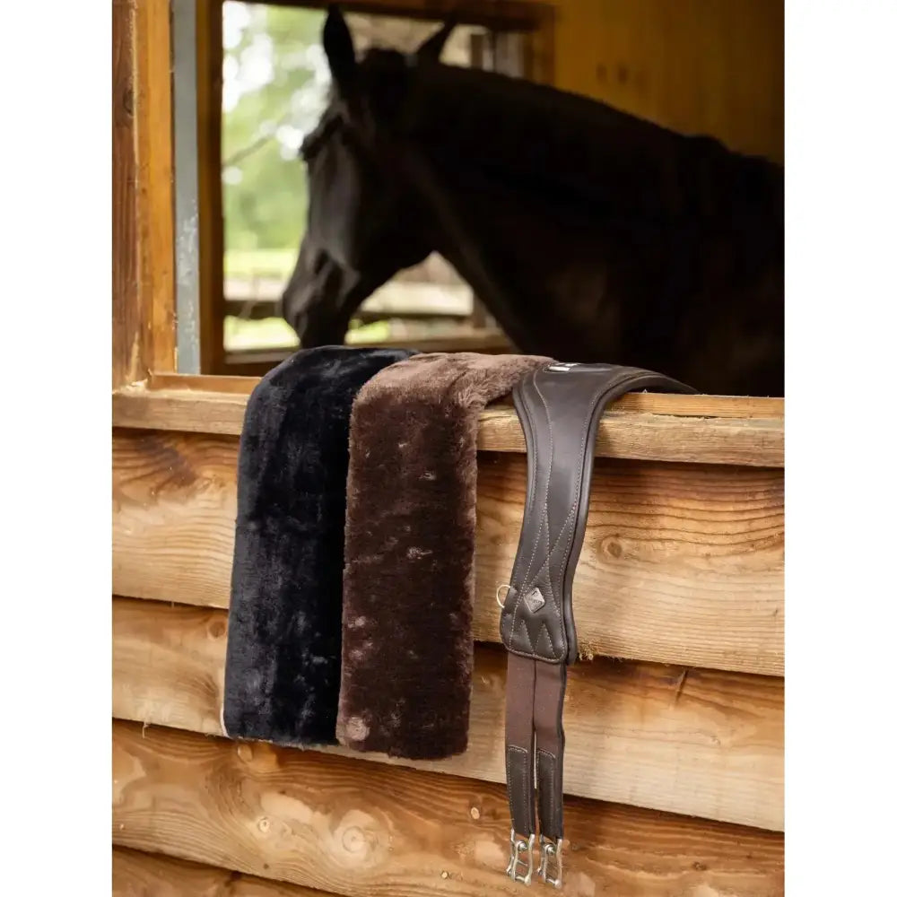 Black and brown lemieux simuwool horse saddle pads with cushioned faux lambswool and leather straps for horse’s comfort
