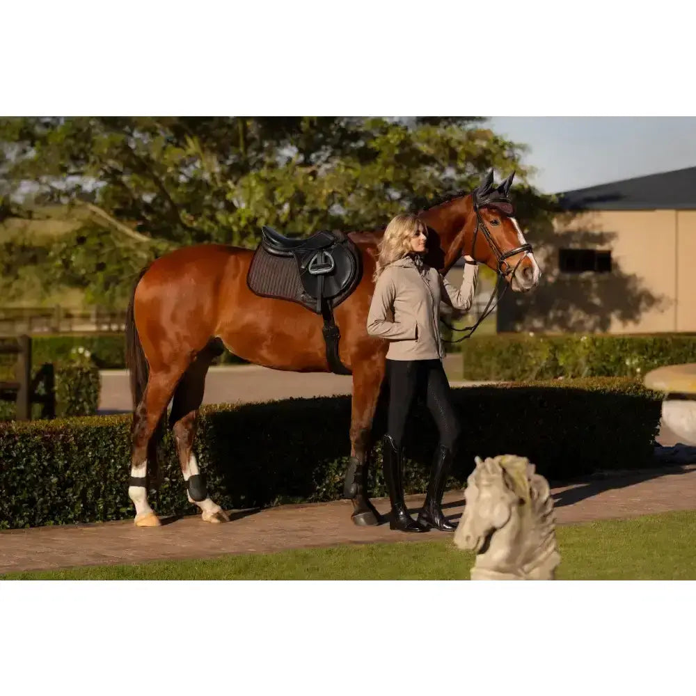 A sleek chestnut horse with a black saddle wearing lemieux suede close contact square cinder saddle pad