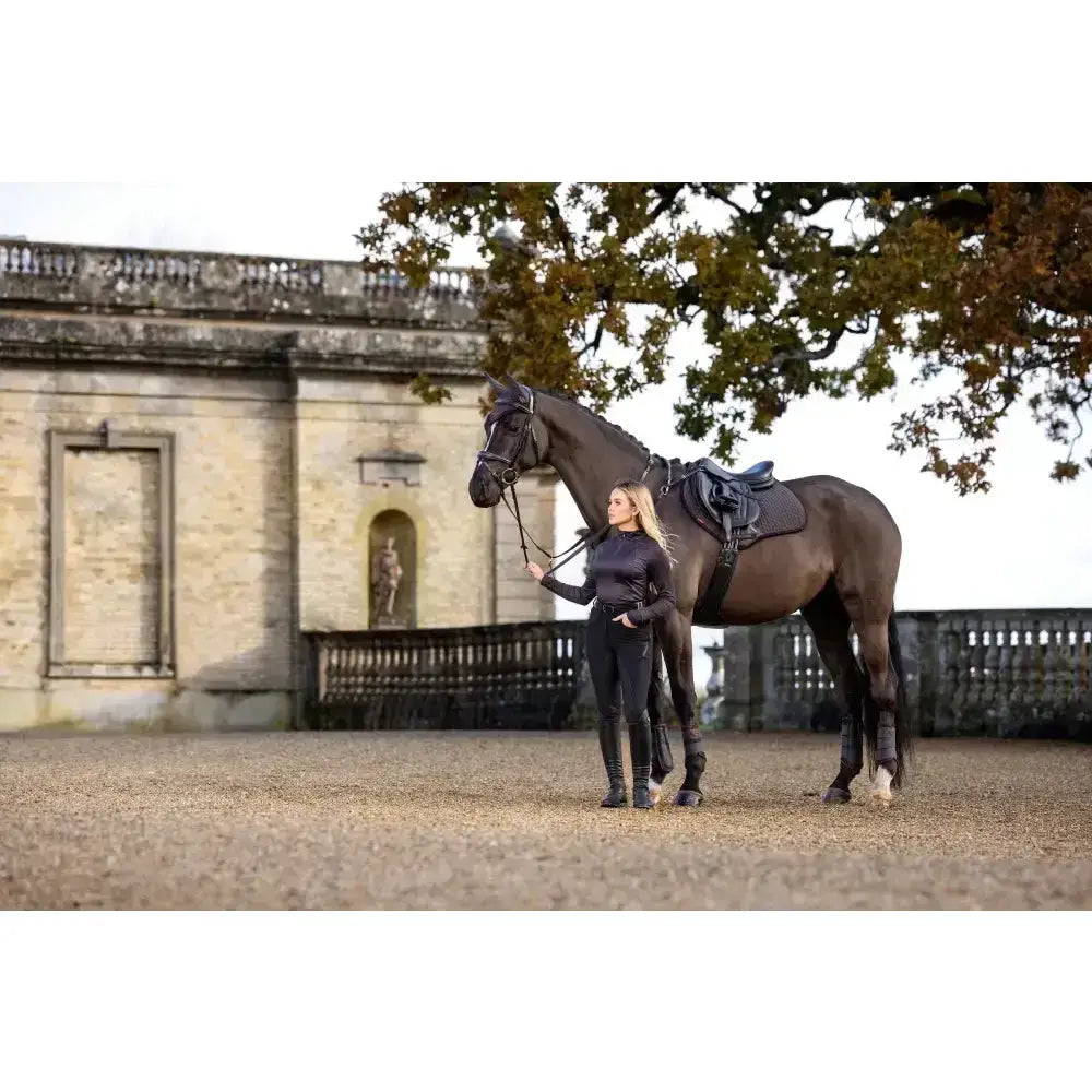 Dark brown horse with black saddle and bridle standing next to woman featuring lemieux suede close contact square cinder saddle pad