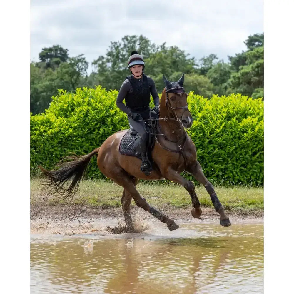 A brown horse with a glossy coat wearing lemieux suede close contact square cinder saddle and dark bridle