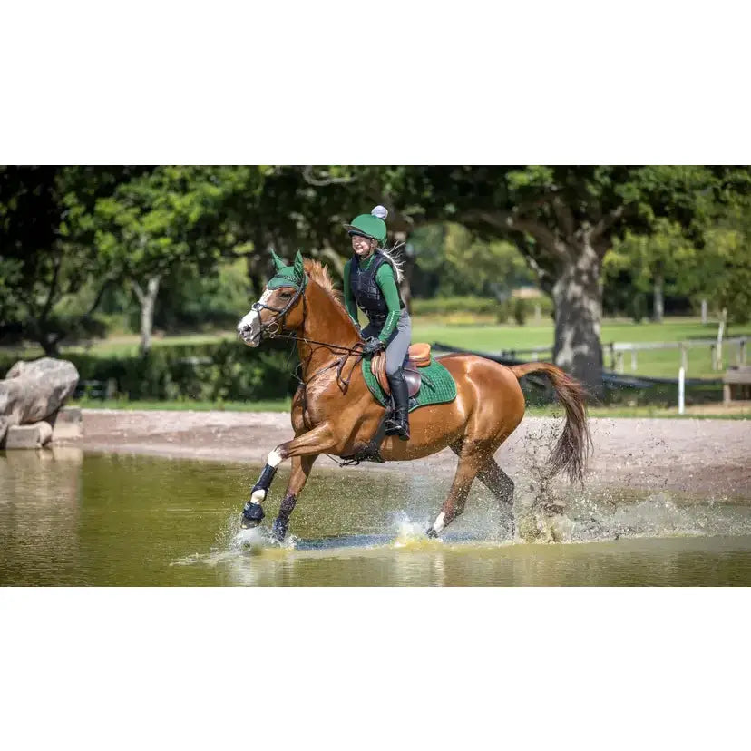 A chestnut horse galloping through water wearing lemieux suede close contact square hunter green protective gear