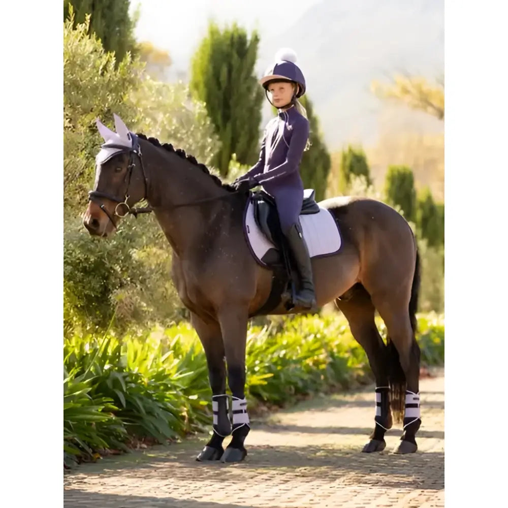 A young rider on a dark brown horse wearing a lemieux suede gp square lilac saddle pad and white protective leg wraps