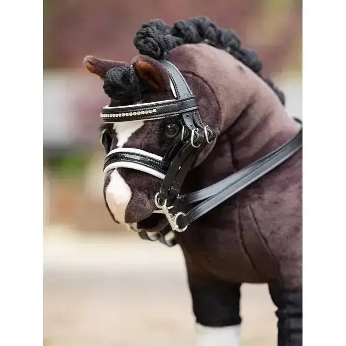 A plush brown lemieux toy pony wearing a black leather double bridle black with silver studs and a braided mane