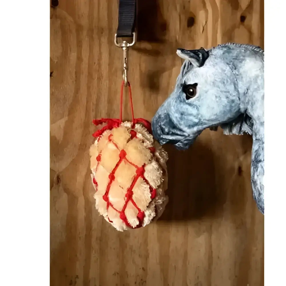A plush light beige lemieux toy pony with a red pony haynet ember hanging from a black strap