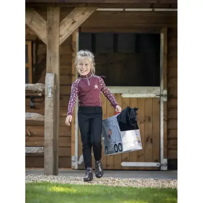 A child carries a silver lemieux toy pony reversible carry case shaped like a toy horse trailer with black mane and wheels