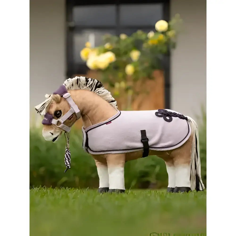 A plush light gray lemieux toy pony wearing a lilac pony rug with black trim and braided details