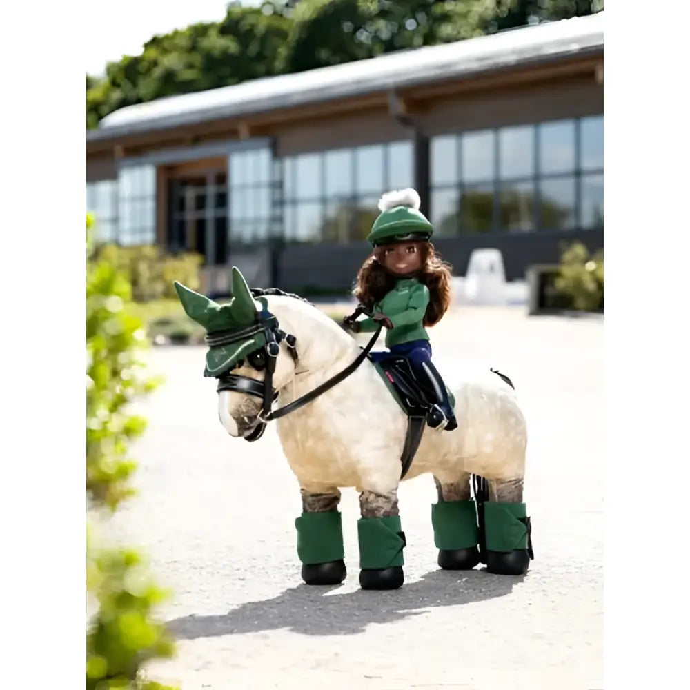 A toy rider maya doll in a green outfit rides a cream horse figurine with dark green wraps lemieux toy rider