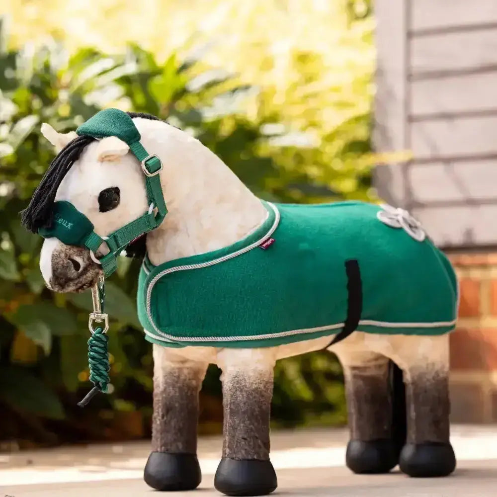 A plush white toy horse wearing a lemieux toy rugs evergreen quality fleece toy rug and matching green bridle