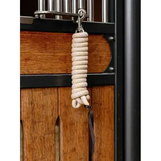 Coiled beige lemieux training leadrope blossom with metal hook and dark strap hanging from stable gate