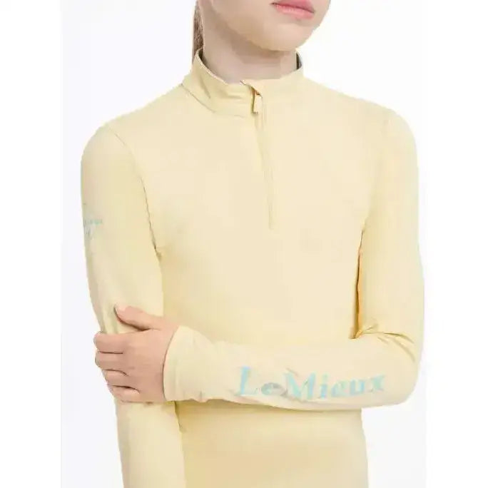 A pale yellow lemieux young rider base layer mimosa with long sleeves and a quarter-zip collar and logo on the sleeve