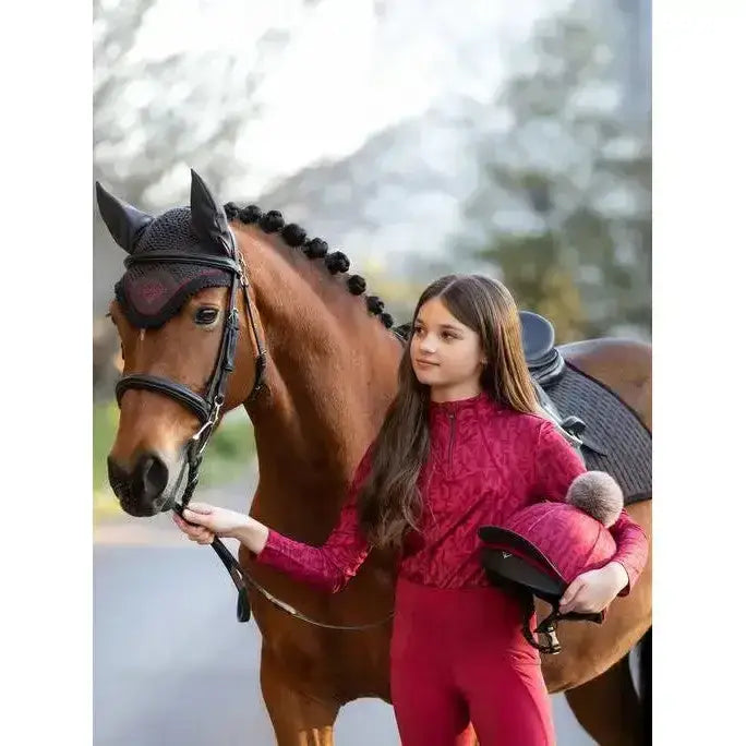 The girl wears a vibrant red long-sleeved lace lemieux young rider casey base layer ember with matching leggings