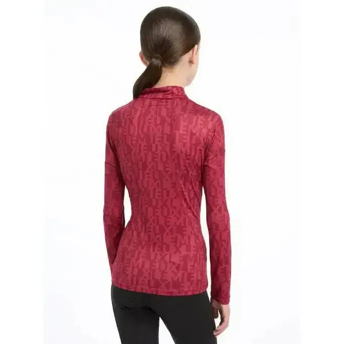 A woman wearing a red lemieux young rider casey base layer ember long-sleeved top with subtle duche pattern