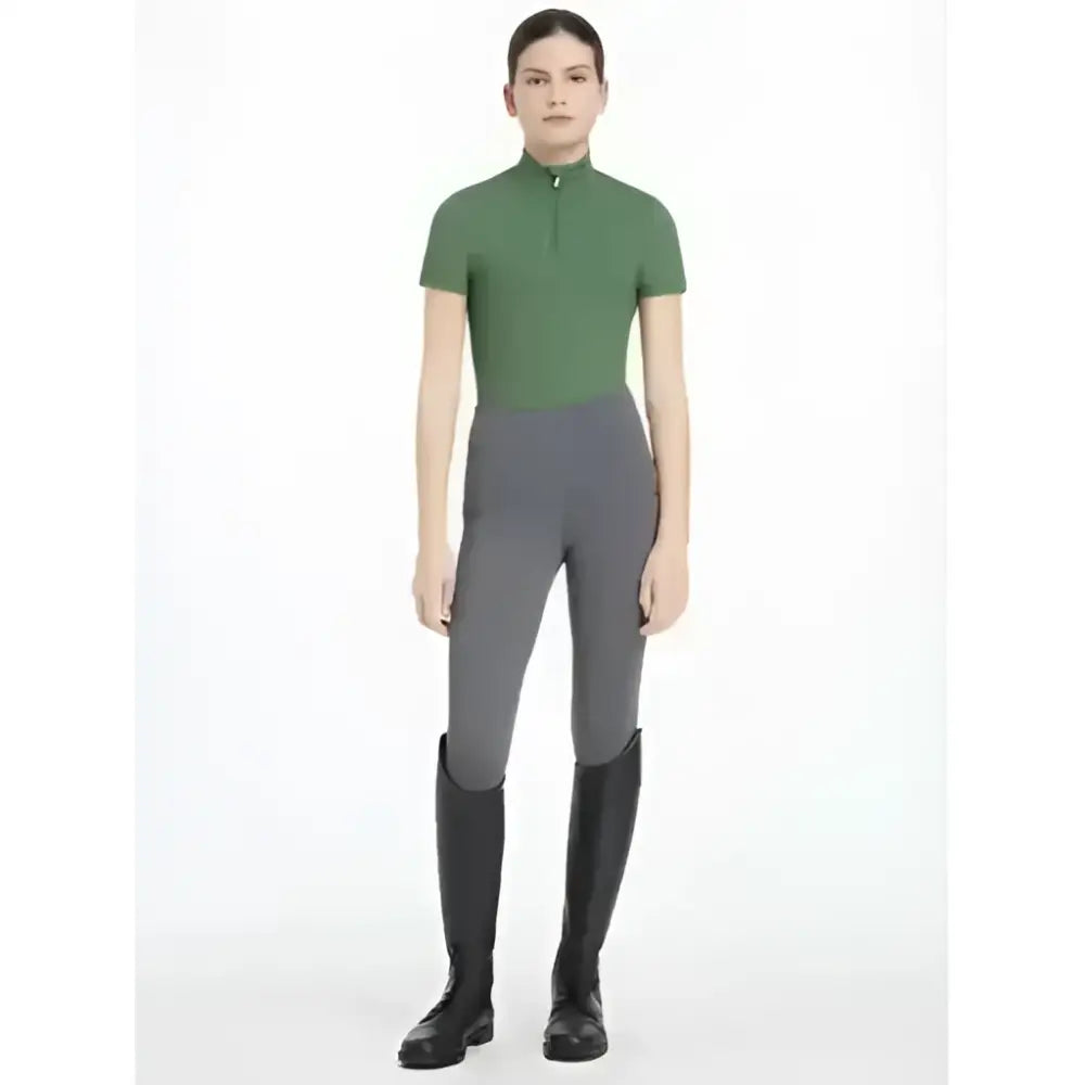 A woman wears a lemieux young rider classic short sleeve base layer in hunter green with black riding boots