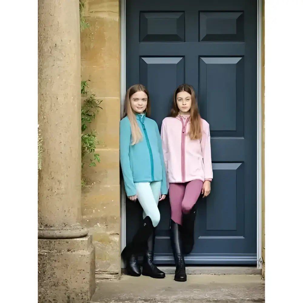 Two young girls in matching lemieux young rider felicity fleece zip soft lagoon blue equestrian jackets and leggings