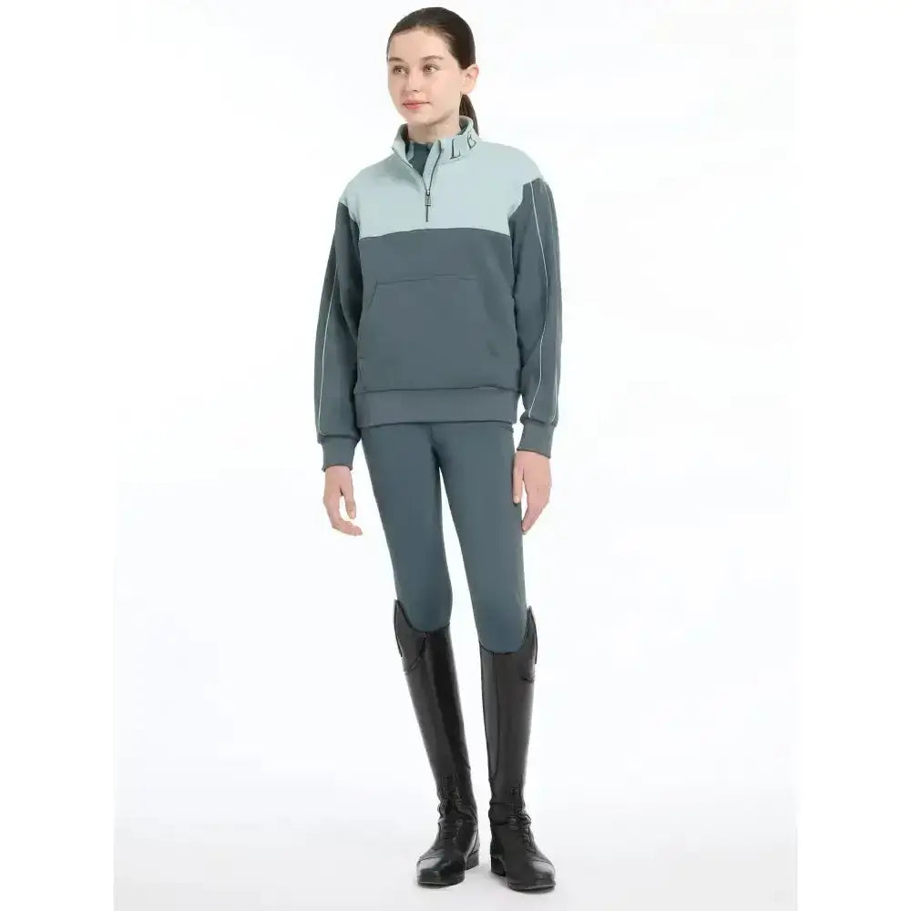 A woman wearing a lemieux young rider kate quarter zip soft fleece zip sweat petrol and glacier color panels
