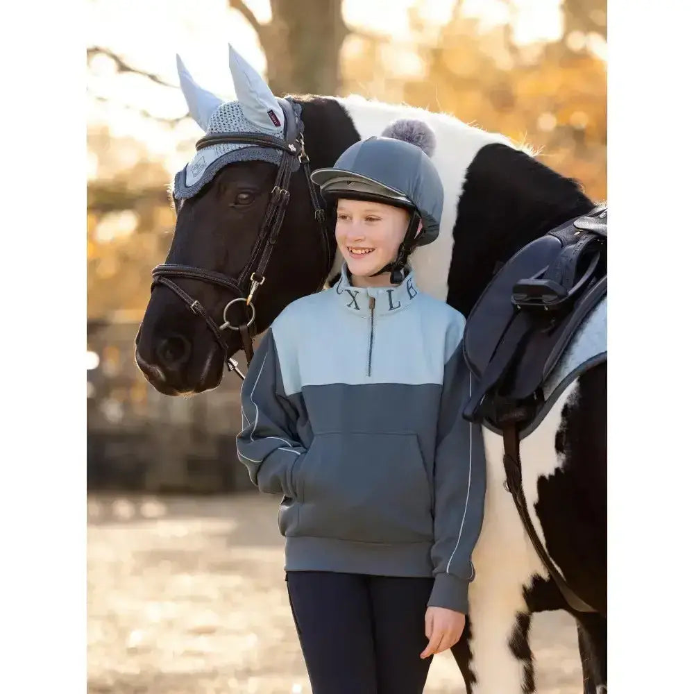 A child wearing a lemieux young rider kate quarter zip zip sweat petrol in gray and light blue with white piping details