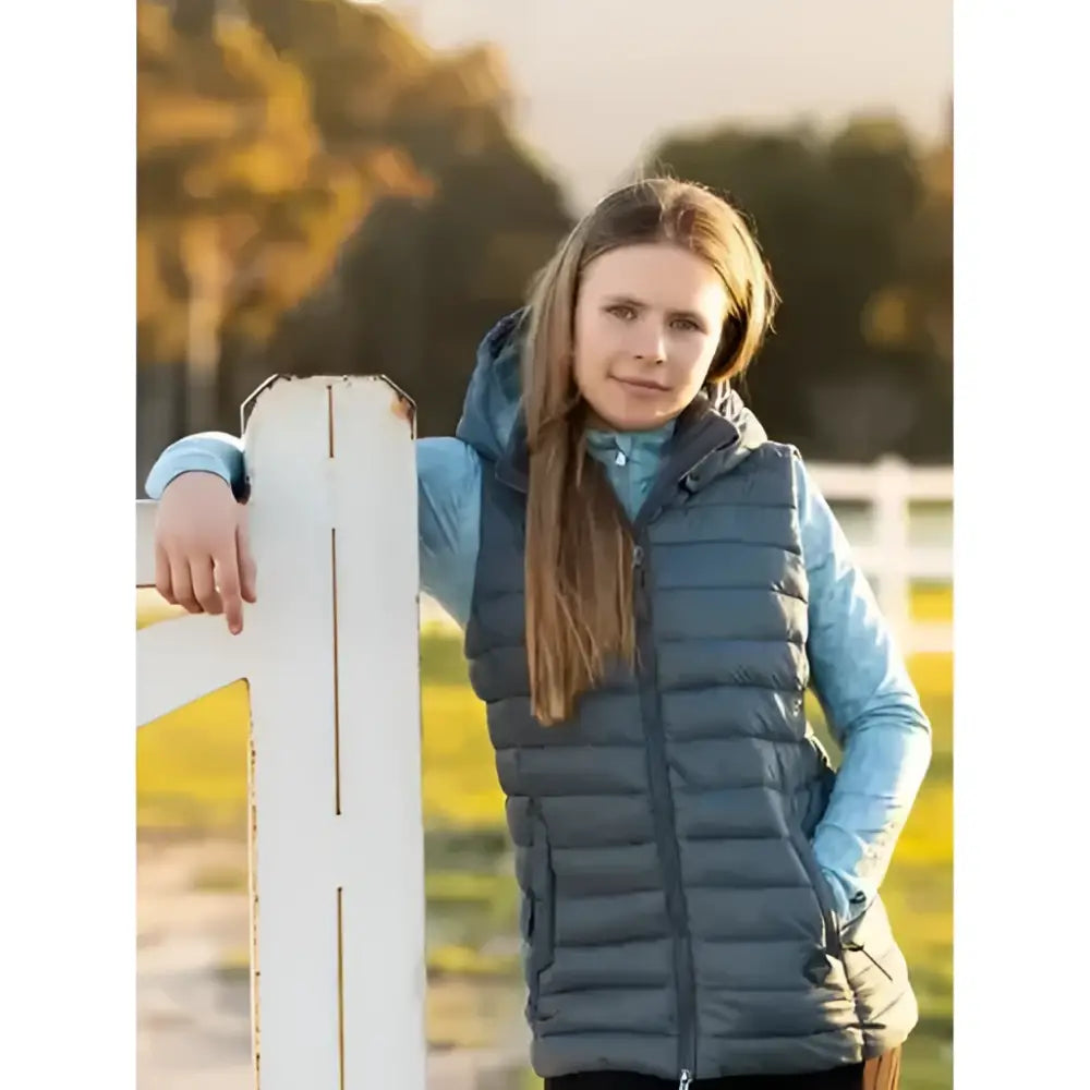 A young girl wearing a dark blue quilted lemieux young rider milly puffer gilet petrol over a light blue shirt