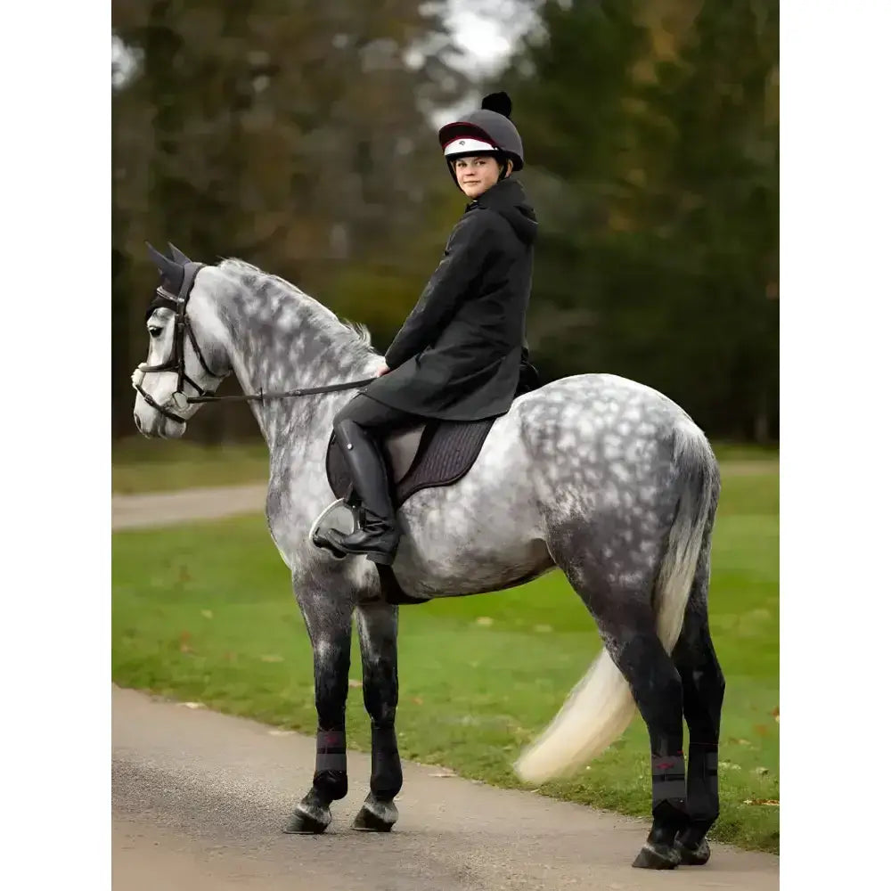 A dapple gray horse with white mane and tail wearing lemieux young rider skye waterproof coat black riding gear