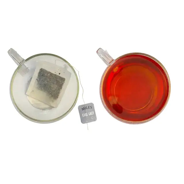 A clear glass teacup with amber earl grey tea and a loose leaf miles tea earl grey envelope with italian bergamot oil