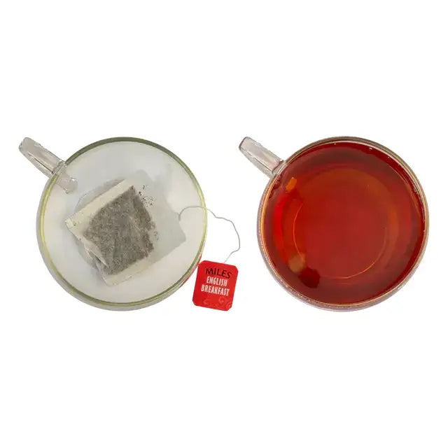 Red tea bag labeled miles english breakfast sits next to clear glass mug of brewed english breakfast envelope tea from kenya tea leaves