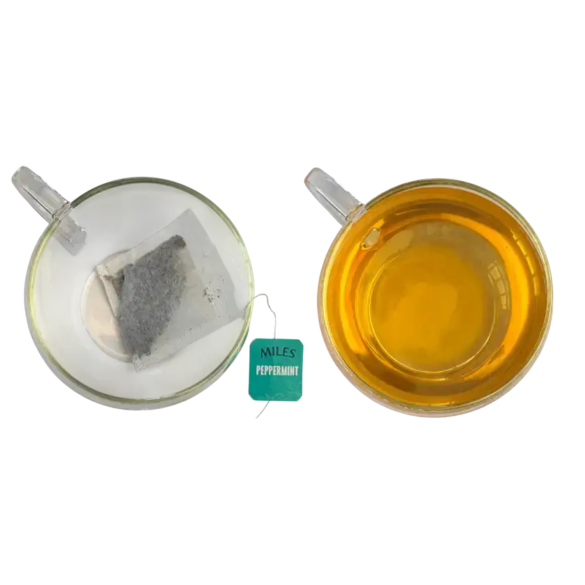 Two clear glass teacups with miles tea envelope peppermint teabags brewed golden yellow tea and real peppermint leaves