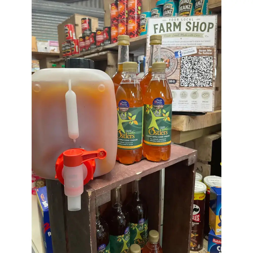 Translucent plastic dispenser with red spigot filled with amber ostlers cider organic apple cider vinegar mother refills north devon