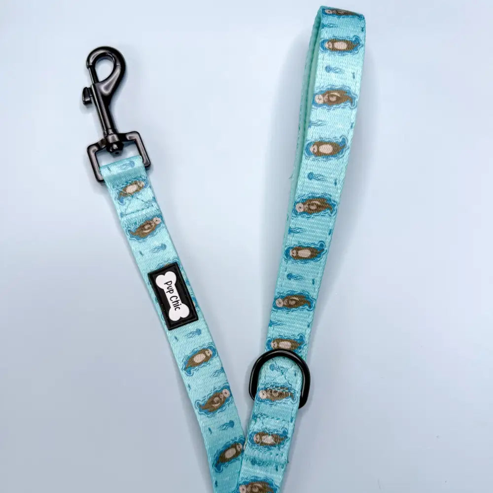 A light teal otterly lovely 5ft dog lead with sea otters pattern, black metal hardware, and branded tag