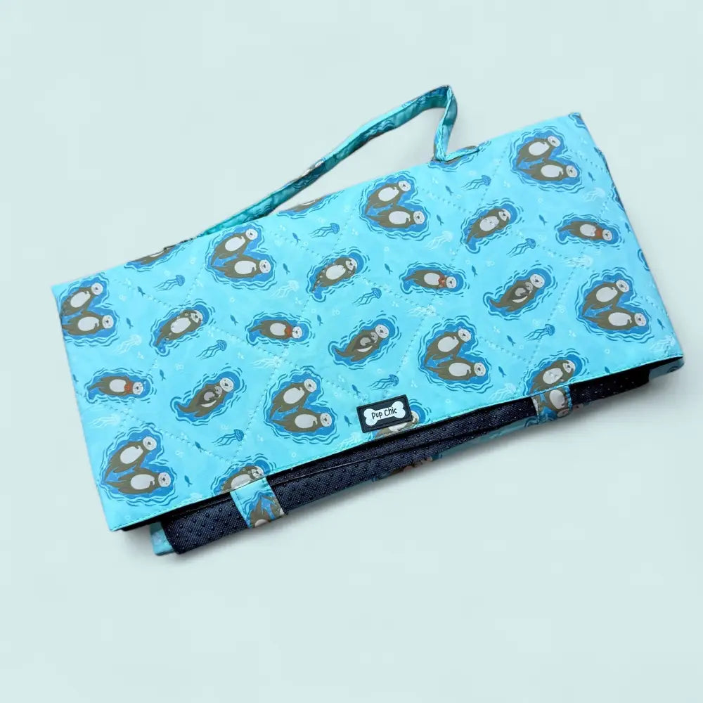 A light blue fabric pet carrier from the otterly lovely collection with cartoon otters is the perfect travel mat for dog comfortable trips