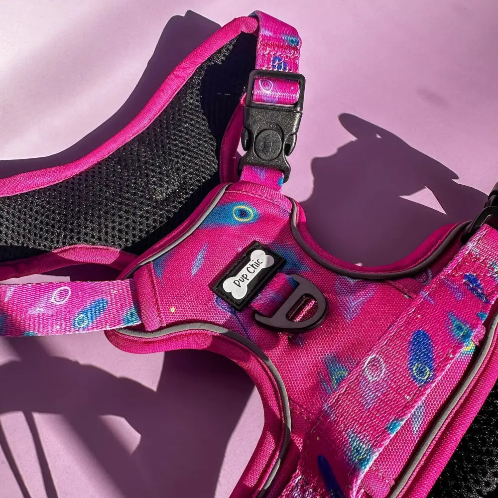 A vibrant pink tactical dog harness with cosmic blue white circles black mesh padding and a pip chic tag peacock power design