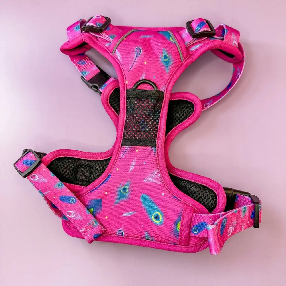 A vibrant pink tactical dog harness with breathable black mesh and a playful blue green peacock feather print for pup chic style