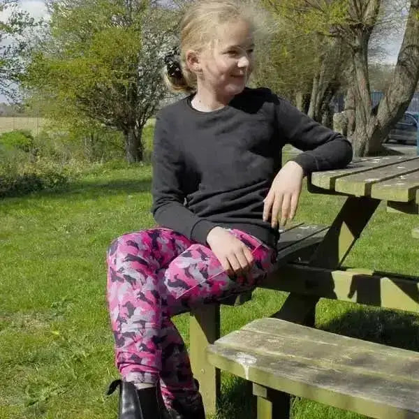A young girl wearing vibrant pink and black pony print riding tights rhinegold perfect for junior horse riders