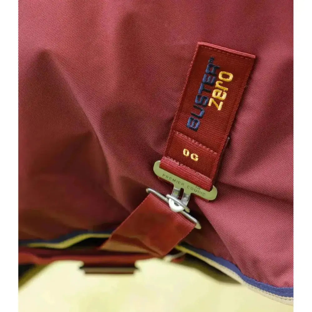 Red fabric strap with buster zero embroidered in gold and blue, attached to metallic buckle on premier equine buster turnout rug made from denier ballistic nylon