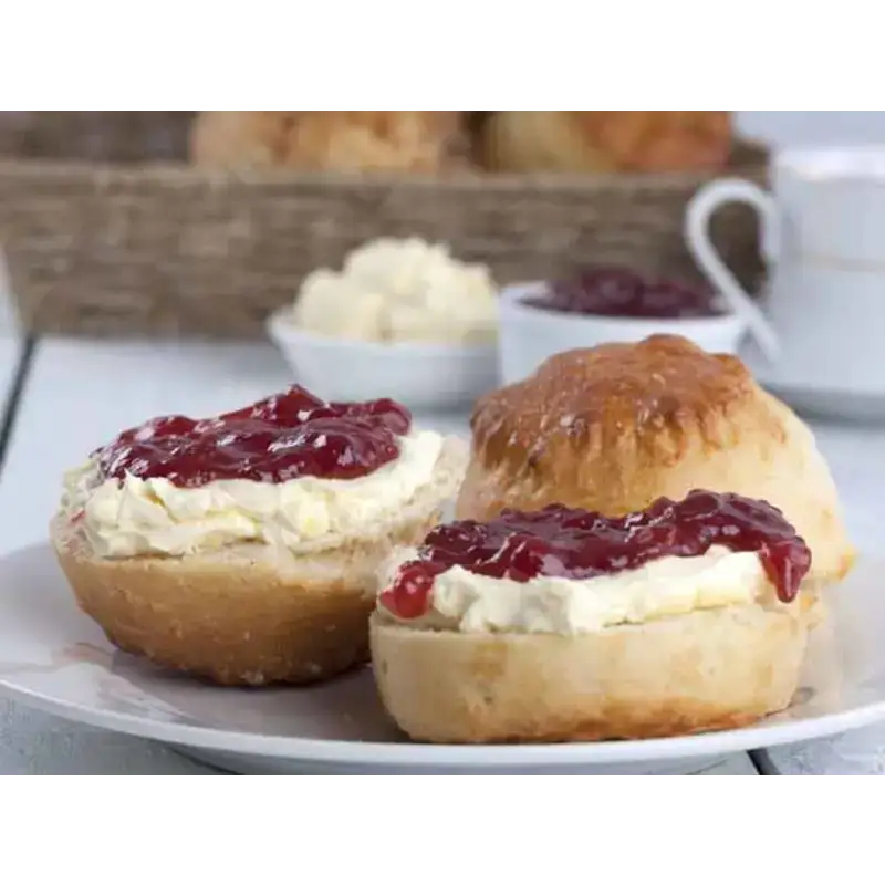 Golden-brown proper devon scone halves topped with creamy clotted cream and red jam on a white plate
