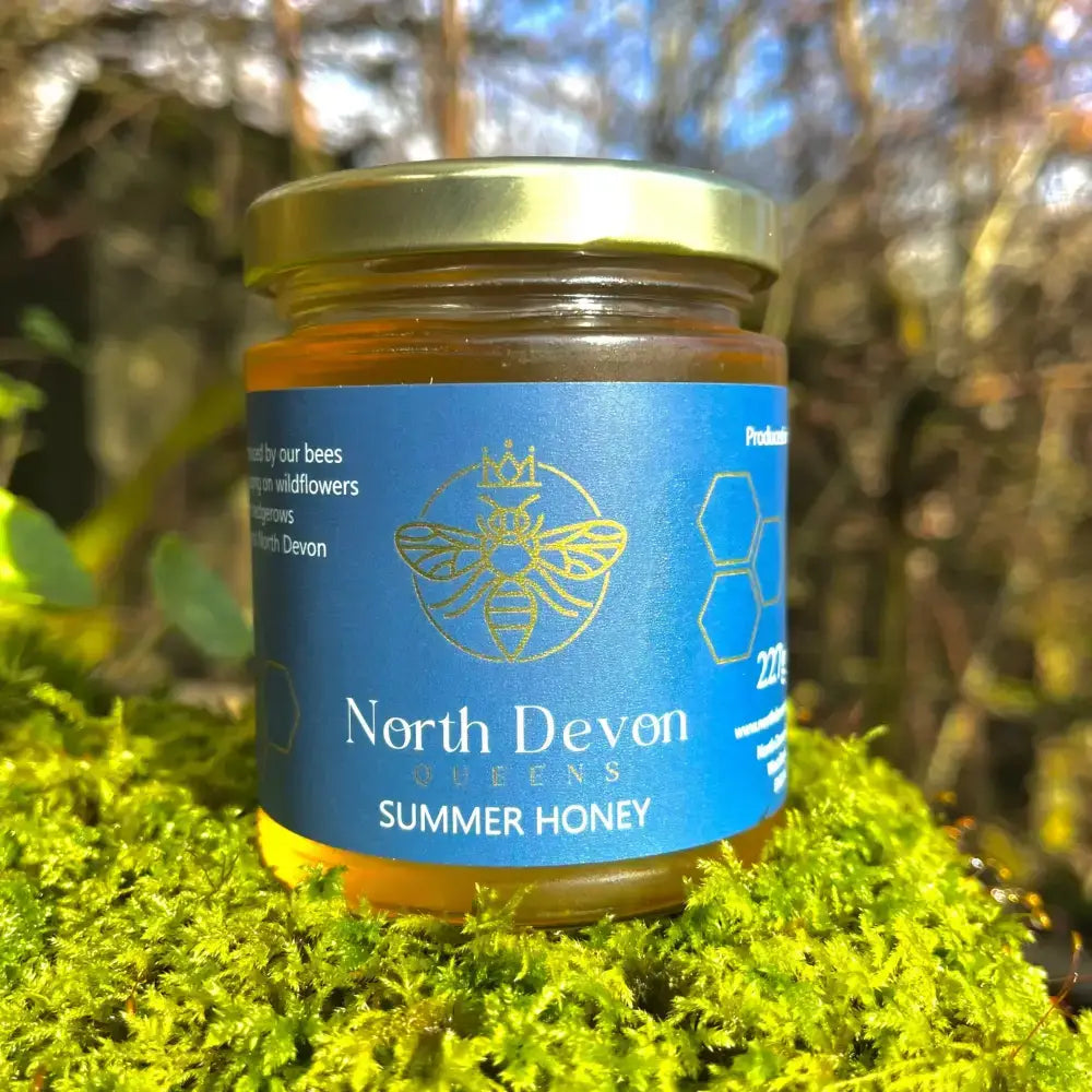 A jar of queens north devon small batch summer honey with golden lid blue label and amber honey inside