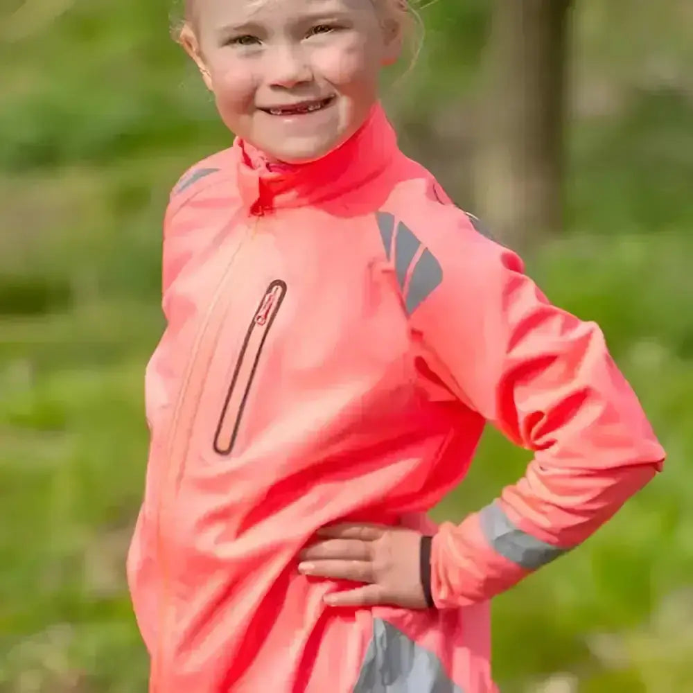 A bright coral pink reflector children’s jacket by hy equestrian with gray reflective panels for darker evenings wearing