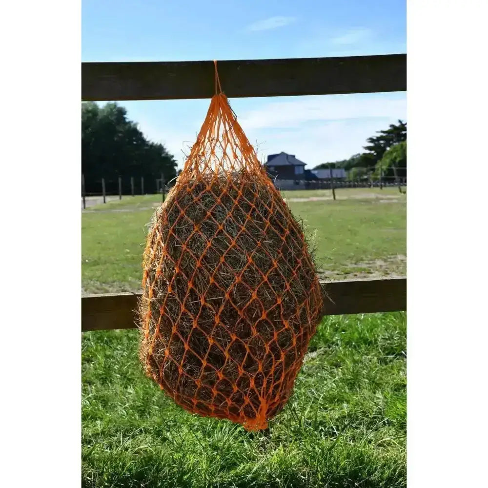 Orange mesh rhinegold monarch slow feeder haynet with small holes hanging on wooden fence filled with hay
