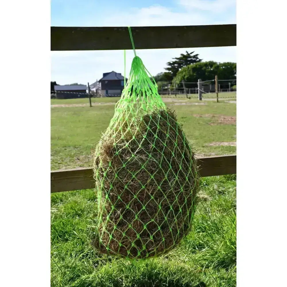 Bright green rhinegold monarch slow feeder haynet small hole made of mesh hanging from wooden fence filled with dry grass
