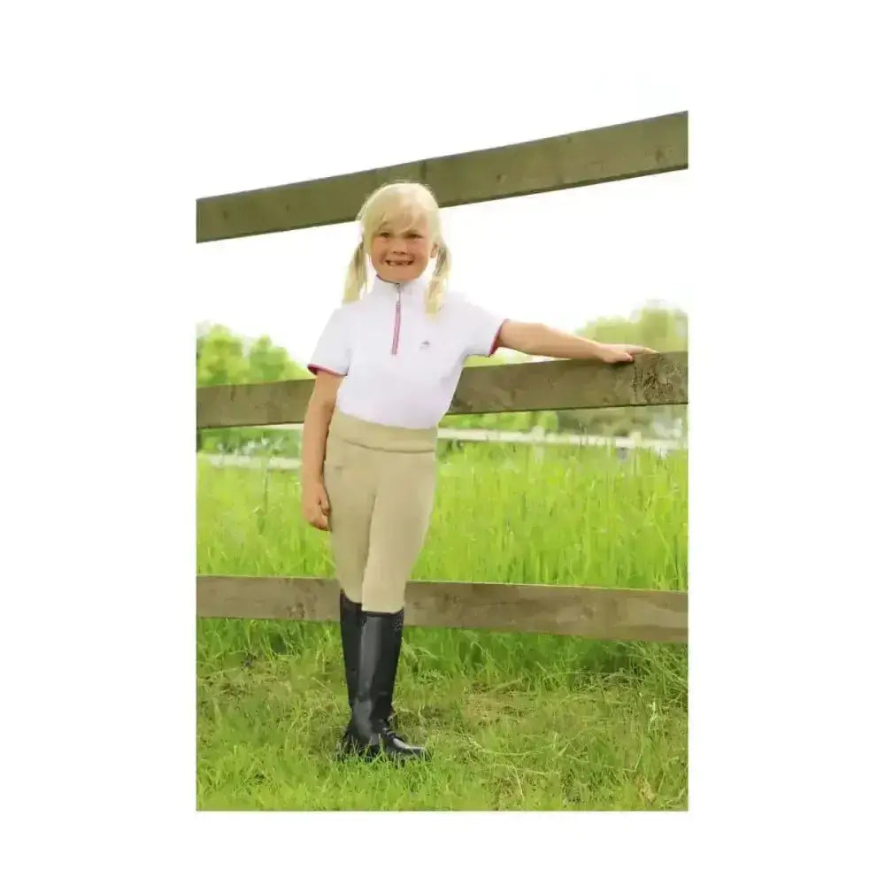 A young girl wearing sara riding tights in beige with a white polo shirt and black boots perfect for aspiring equestrian athlete