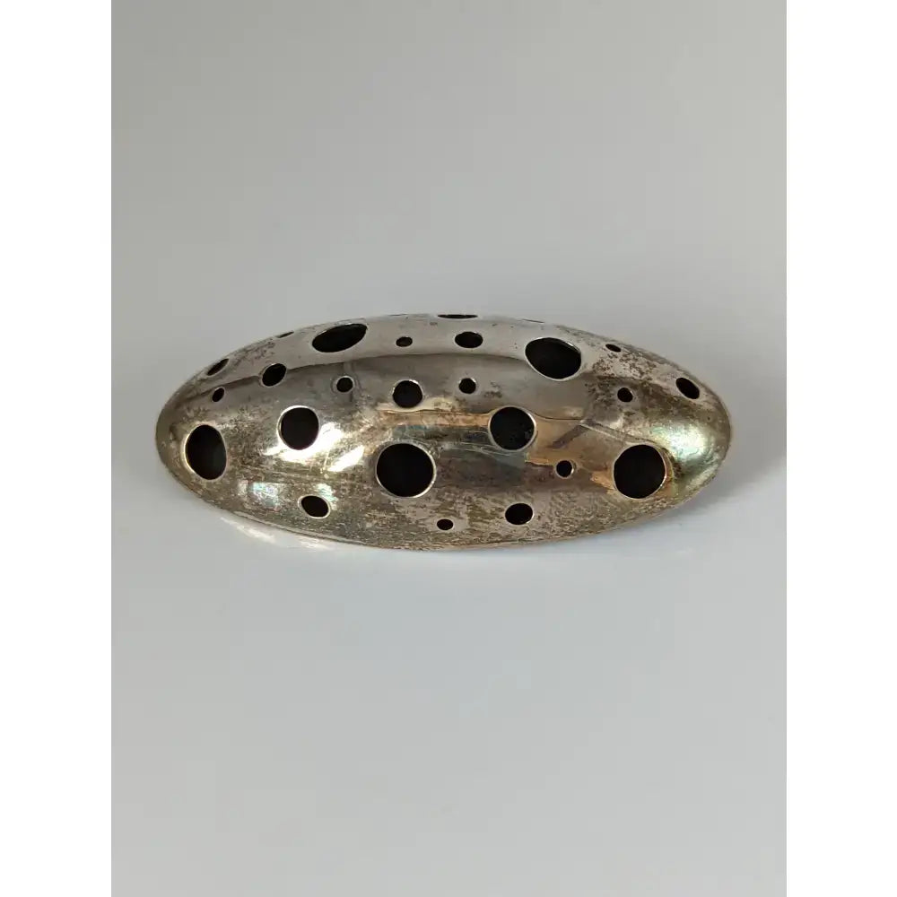 Silver steed coral silver brooch with oval textured metal design and multiple circular holes in silver tone